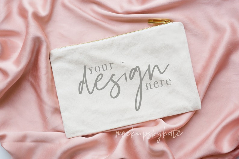 May include: White canvas zipper pouch with a gold zipper pull. The pouch is lying on a pink satin fabric and has the text "Your design here" printed on it.