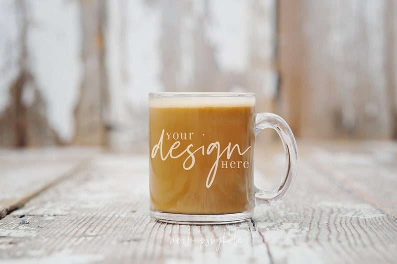 Op de afbeelding: Een heldere glazen mok met een handvat gevuld met een lichtbruine vloeistof. De mok heeft de tekst "Your design here" aan de zijkant gedrukt.