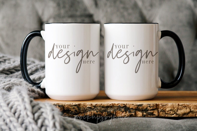 May include: Two white ceramic mugs with black handles and black rims. The mugs are sitting on a wooden surface and have the text "Your design here" printed on them.