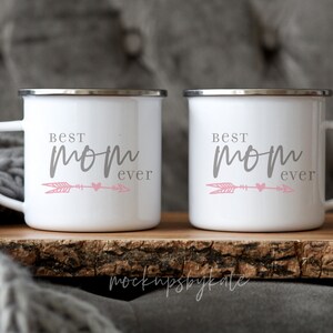 May include: Two white enamel mugs with a gray inscription that reads "Best Mom Ever" and a pink arrow and heart design.