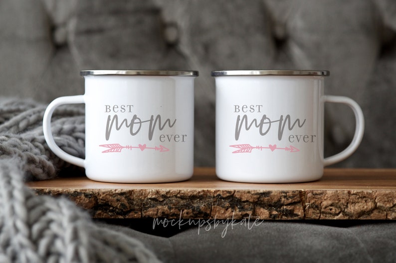 May include: Two white enamel mugs with a gray inscription that reads "Best Mom Ever" and a pink arrow and heart design.