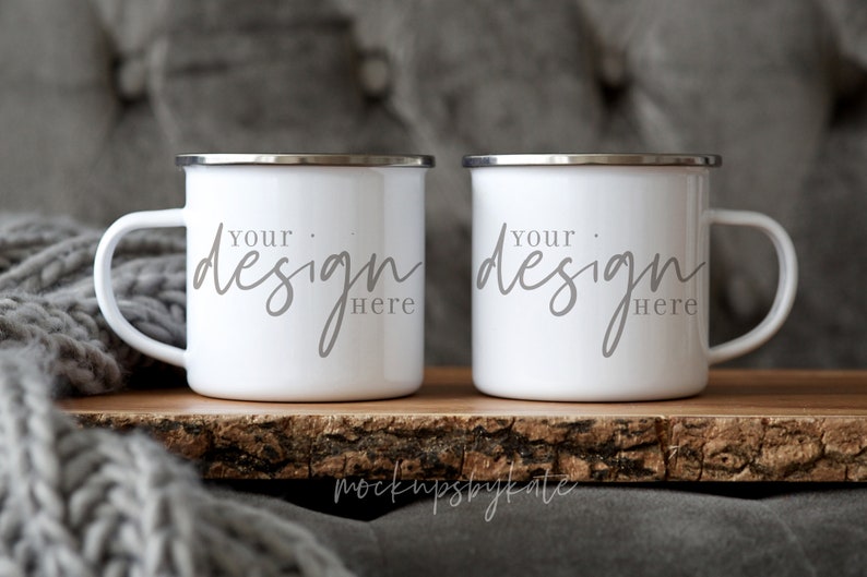 May include: Two white enamel mugs with silver rims and handles. The mugs are on a wooden surface and have the text "Your design here" written on them.