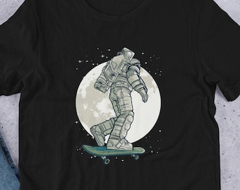 Puede incluir: Camiseta negra con un gráfico de un astronauta patinando sobre la luna. El astronaute lleva un traje espacial blanco y un casco. La luna es de color gris claro con un cráter gris oscuro. El fondo es de color azul oscuro con estrellas blancas.