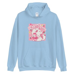 K&ouml;nnte beinhalten: Hellblauer Kapuzenpullover mit einem Cartoon-Katzen-Design, das Erdbeermilch trinkt. Die Grafik enth&auml;lt japanischen Text, Erdbeeren und Sterne. Der Hoodie hat eine Vordertasche und eine Kapuze.