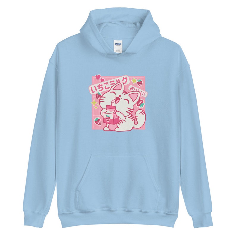 K&ouml;nnte beinhalten: Hellblauer Kapuzenpullover mit einem Cartoon-Katzen-Design, das Erdbeermilch trinkt. Die Grafik enth&auml;lt japanischen Text, Erdbeeren und Sterne. Der Hoodie hat eine Vordertasche und eine Kapuze.
