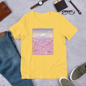 Puede incluir: Camiseta amarilla de manga corta con un gr&aacute;fico de Mount Fuji y flores de cerezo rosas.