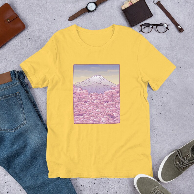 Puede incluir: Camiseta amarilla de manga corta con un gr&aacute;fico de Mount Fuji y flores de cerezo rosas.