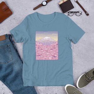Puede incluir: Una camiseta azul claro con un gr&aacute;fico del Monte Fuji en el fondo y flores de cerezo rosas en primer plano.