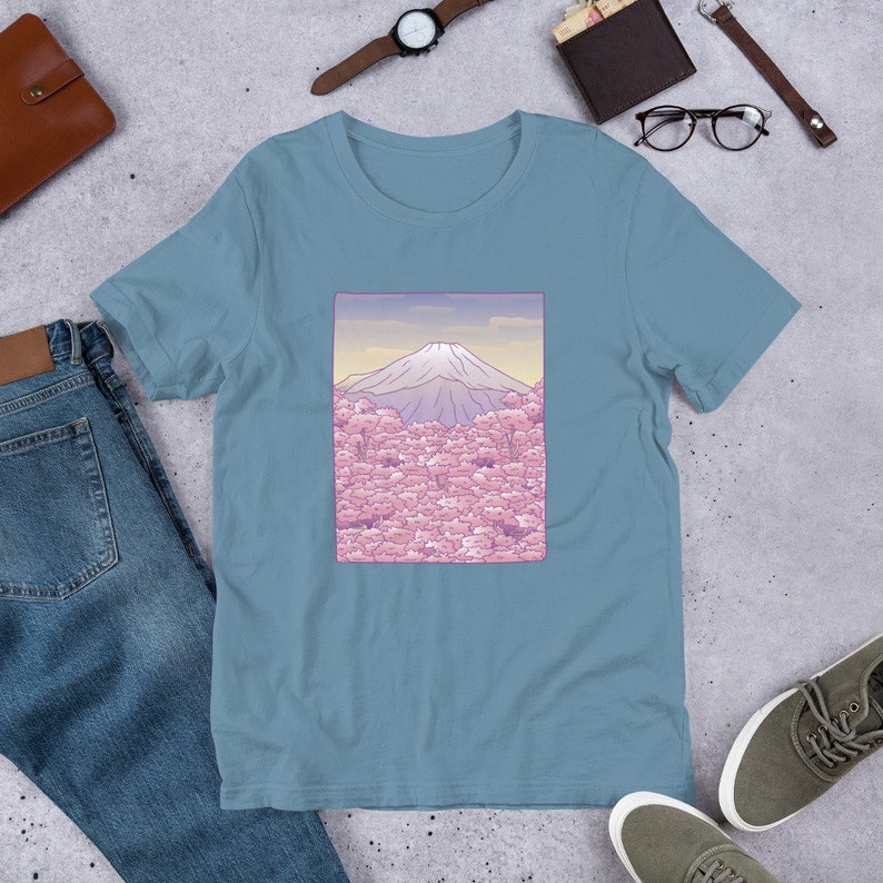 Puede incluir: Una camiseta azul claro con un gr&aacute;fico del Monte Fuji en el fondo y flores de cerezo rosas en primer plano.