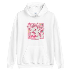 K&ouml;nnte beinhalten: Wei&szlig;er Kapuzenpullover mit einem rosa Aufdruck einer Katze, die Erdbeermilch trinkt. Die Grafik enth&auml;lt japanischen Text, Erdbeeren und Sterne. Der Hoodie hat eine Vordertasche und eine Kapuze mit Kordelzug.