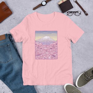 Puede incluir: Camiseta rosa con un gr&aacute;fico de Mount Fuji y flores de cerezo en una paleta de colores pastel.