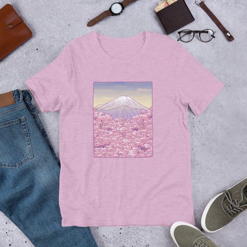 Puede incluir: Una camiseta rosa con un gr&aacute;fico del Monte Fuji en el fondo con flores de cerezo rosas en primer plano. El gr&aacute;fico est&aacute; enmarcado en un rect&aacute;ngulo morado claro.