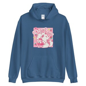 K&ouml;nnte beinhalten: Blauer Kapuzenpullover mit einem rosa quadratischen Grafikdesign. Das Design zeigt eine Cartoon-Katze, die Erdbeermilch trinkt, mit japanischem Text, Erdbeeren und Sternen. Der Hoodie hat eine Vordertasche und eine Kapuze.