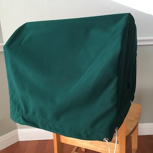 May include: A dark green fabric cover for a large piece of furniture or equipment. The cover has a drawstring closure and is sitting on a wooden chair.