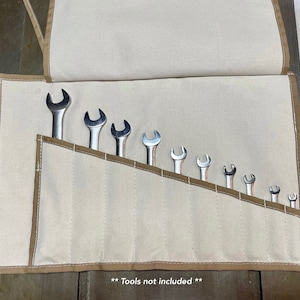 May include: A beige canvas tool roll with brown stitching and 10 slots for holding wrenches. The text "**Tools not included**" is printed on the bottom of the roll.