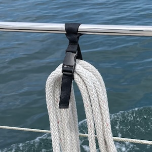 May include: A black strap with a buckle is attached to a metal railing. A white rope with red threads is looped through the strap.