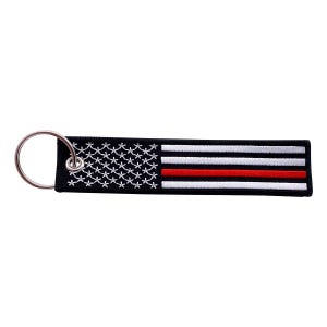 May include: Embroidered keychain featuring a design inspired by the American flag. The black rectangle has white stars and stripes, with a single red stripe. A silver metal ring is attached for keys.