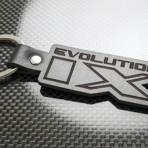 May include: A black leather keychain with a silver key ring. The keychain has a gray leather tag with the word "EVOLUTION" and a stylized "X" design.