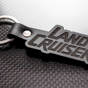 May include: Black leather keyring with a silver key ring and the words "LAND CRUISER" embossed in black.