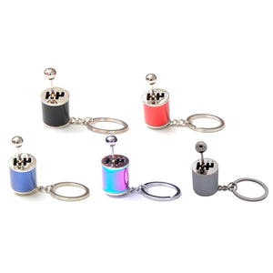 May include: Five miniature car gear shift keychains in black, red, blue, iridescent, and gray. Each keychain features a silver gear shift lever and a silver key ring. The keychains are designed to resemble a car's gear shift.