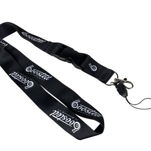 Puede incluir: Lanyard negro con un logotipo plateado 'Boosted Status' y un gráfico de turbocompresor. El lanyard tiene un clip de plástico negro y un gancho de metal plateado.