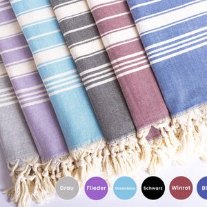Puede incluir: Una colecci&oacute;n de toallas de playa a rayas en varios colores: gris, morado, azul claro, negro, burdeos y azul. Cada toalla tiene flecos blancos y rayas horizontales. Los nombres de los colores est&aacute;n abajo.