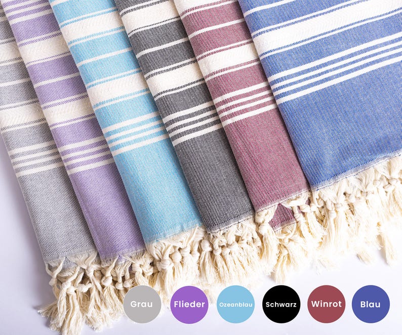 Puede incluir: Una colecci&oacute;n de toallas de playa a rayas en varios colores: gris, morado, azul claro, negro, burdeos y azul. Cada toalla tiene flecos blancos y rayas horizontales. Los nombres de los colores est&aacute;n abajo.