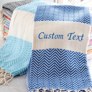 May include: A stack of Turkish towels with a herringbone pattern in blue and white. The top towel has the text "Custom Text" embroidered on it.