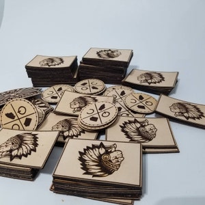 Puede incluir: Una colecci&oacute;n de parches de madera cortados con l&aacute;ser que presentan tocados de nativos americanos y dise&ntilde;os geom&eacute;tricos. Los parches est&aacute;n apilados en pilas y dispuestos sobre una superficie blanca.