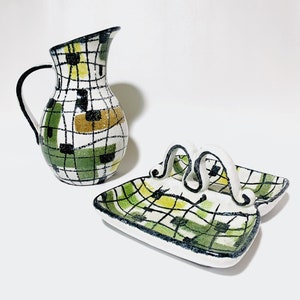 May include: A ceramic pitcher and serving dish set. The pitcher has a black handle and a white base with a green, black, and gold grid pattern. The serving dish has two handles and a matching pattern.
