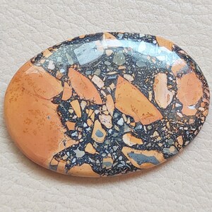Puede incluir: Primer plano de una piedra lisa de forma ovalada con un patr&oacute;n &uacute;nico de negro, naranja y blanco. La piedra tiene un acabado pulido y es una muestra natural y colorida.