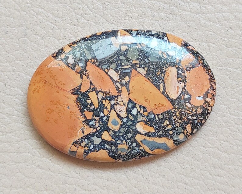Puede incluir: Primer plano de una piedra lisa de forma ovalada con un patr&oacute;n &uacute;nico de negro, naranja y blanco. La piedra tiene un acabado pulido y es una muestra natural y colorida.