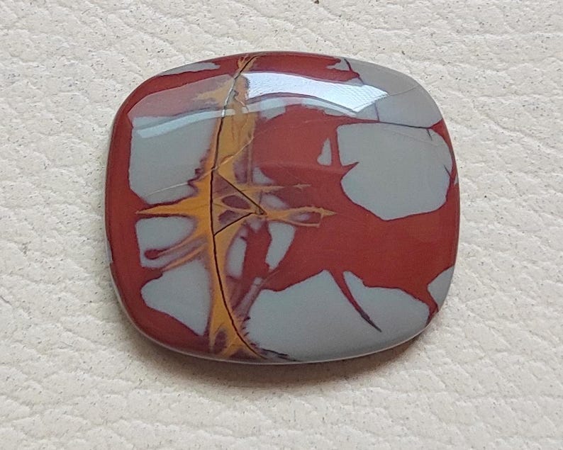 Pu&ograve; includere: Un cabochon quadrato in diaspro lucido, rosso, grigio e oro con un motivo a spirale.