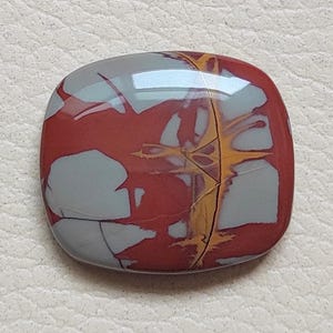 Pu&ograve; includere: Un cabochon di diaspro rosso, grigio e oro con un motivo a spirale unico. Il cabochon &egrave; liscio e lucido e ha una forma leggermente arrotondata.