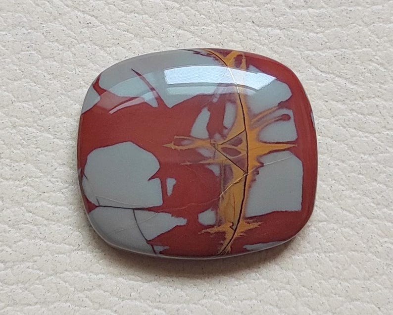 Pu&ograve; includere: Un cabochon di diaspro rosso, grigio e oro con un motivo a spirale unico. Il cabochon &egrave; liscio e lucido e ha una forma leggermente arrotondata.