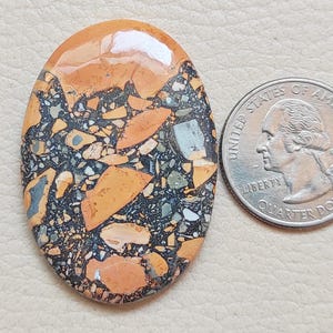 Puede incluir: Primer plano de una piedra ovalada y colorida con un patr&oacute;n de m&aacute;rmol negro, naranja y blanco. La piedra es aproximadamente del tama&ntilde;o de una moneda de 25 centavos.
