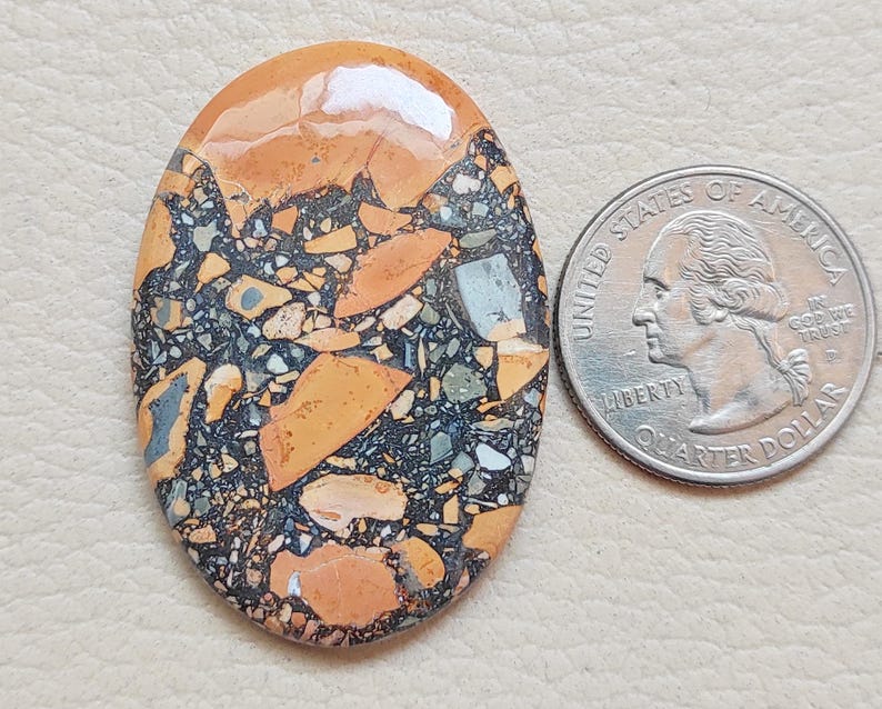 Puede incluir: Primer plano de una piedra ovalada y colorida con un patr&oacute;n de m&aacute;rmol negro, naranja y blanco. La piedra es aproximadamente del tama&ntilde;o de una moneda de 25 centavos.