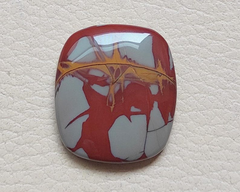 Pu&ograve; includere: Un cabochon di diaspro rosso, grigio e giallo con un motivo astratto unico. Il cabochon &egrave; liscio e lucido, con una finitura lucida.