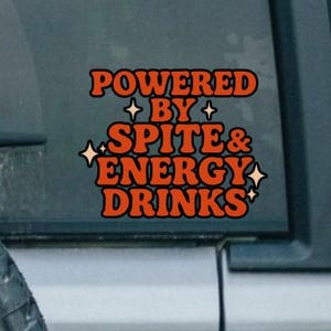 Könnte beinhalten: Ein orangefarbener und weißer Aufkleber auf einer Autoscheibe mit der Aufschrift "POWERED BY SPITE & ENERGY DRINKS". Der Aufkleber befindet sich auf einem grauen Fahrzeug, bei dem ein Ersatzreifen sichtbar ist. Der Ersatzreifen ist schwarz mit weißer Schrift.