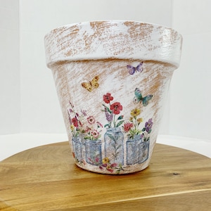 May include: White terracotta flower pot with a distressed finish. The pot features a floral design with butterflies and mason jars filled with flowers.