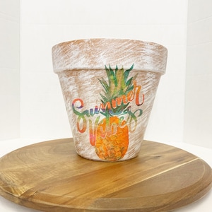 May include: White terracotta planter with a distressed finish. The planter has a colorful pineapple design and the text "Summer Vibes" in a rainbow font.