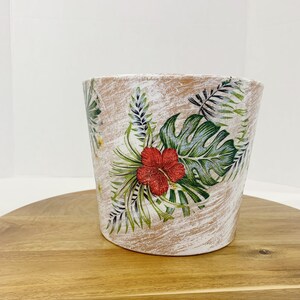 May include: White ceramic planter with a tropical floral design featuring green leaves and a red hibiscus flower. The planter has a distressed white finish.