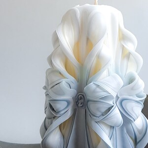 May include: A white and blue carved candle with a decorative bow design. The candle is made of wax and has a smooth, polished finish.