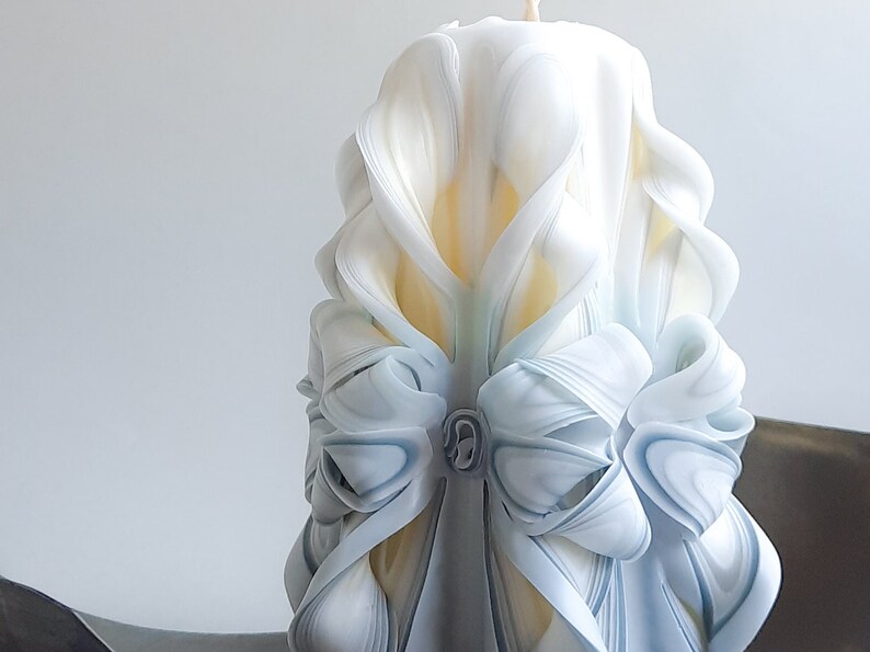 May include: A white and blue carved candle with a decorative bow design. The candle is made of wax and has a smooth, polished finish.