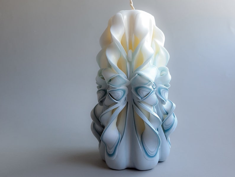 May include: A white and blue carved candle with a decorative design. The candle is shaped like a flower with intricate details.