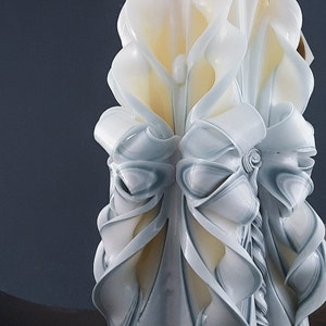 May include: A white and blue carved candle with a decorative design. The candle is shaped like a flower with a large, white bow in the center.