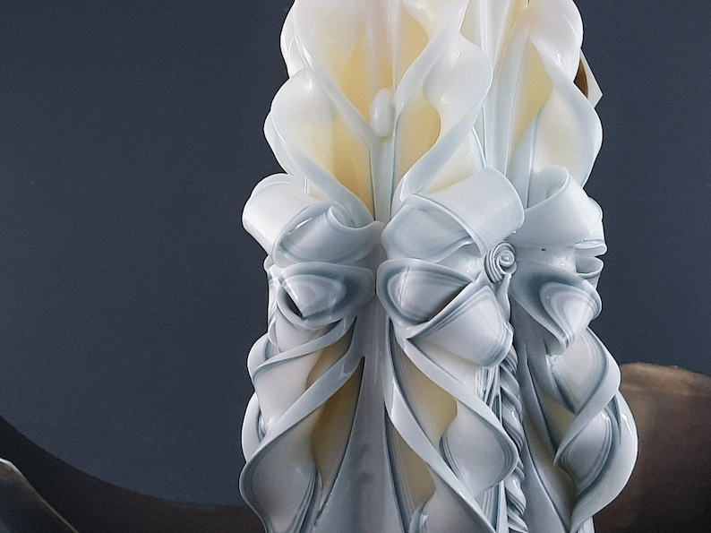 May include: A white and blue carved candle with a decorative design. The candle is shaped like a flower with a large, white bow in the center.