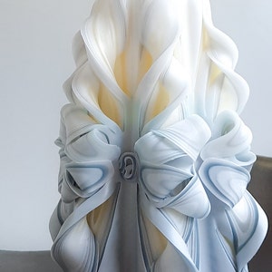 May include: A white and blue carved candle with a decorative bow. The candle is made of wax and has a smooth, polished finish.