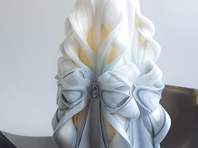 May include: A white and blue carved candle with a decorative bow. The candle is made of wax and has a smooth, polished finish.