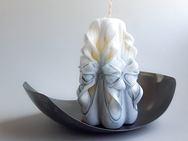 May include: A white and blue carved candle with a decorative bow. The candle is sitting on a black metal tray.